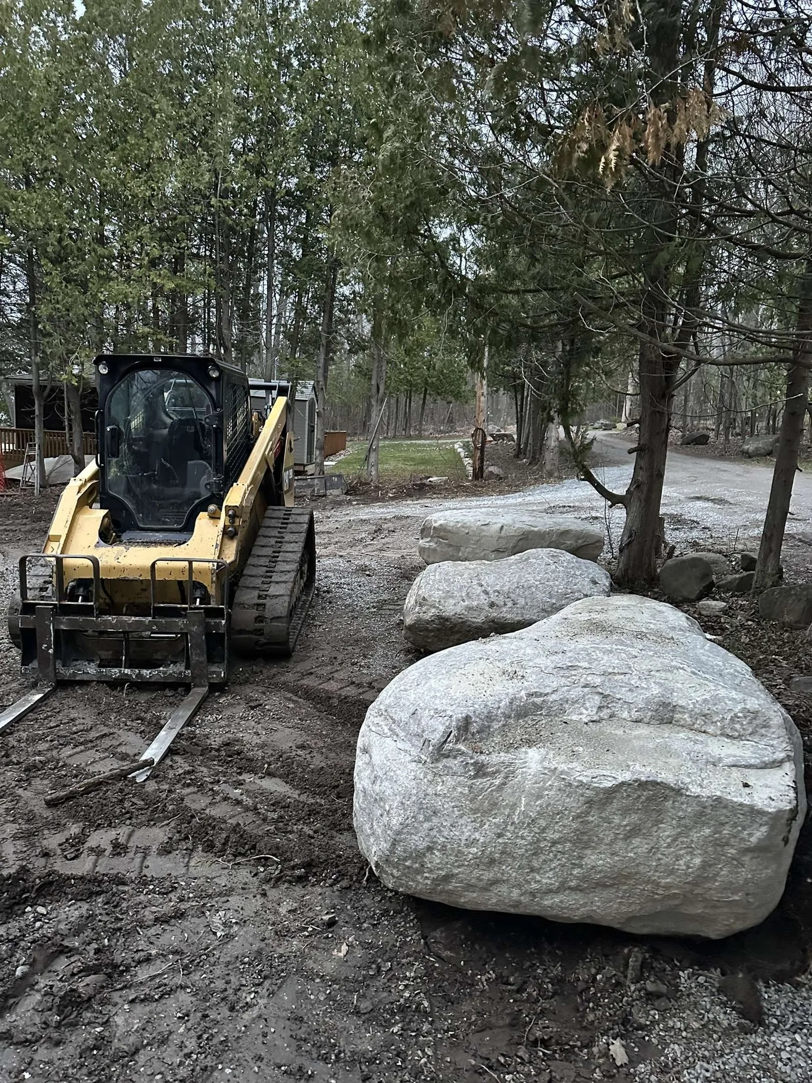 Tracked skid steer moving large rocks between trees