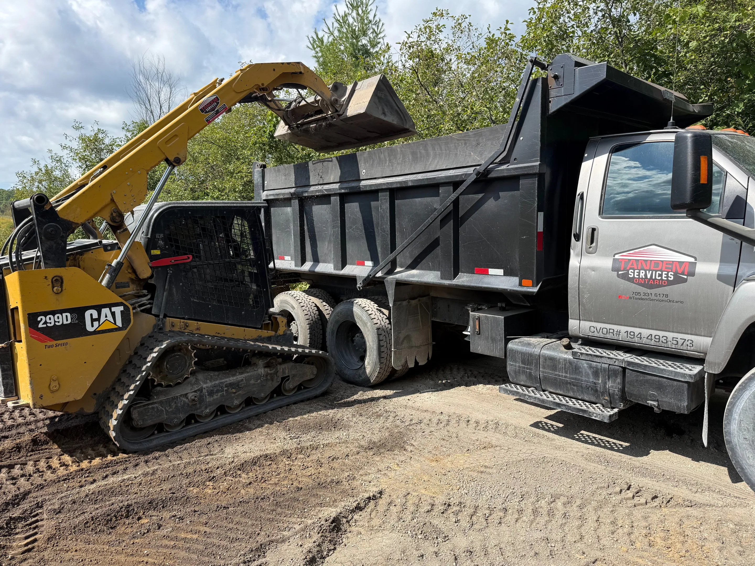 Tracked skid steer loading a Tandem Services dump truck